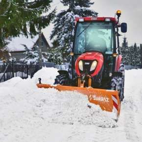 Czerwony mały ciągnik komunalny z pomarańczowym lekkim pługiem odśnieżnym SMART odśnieża chodnik www.korbanek.pl